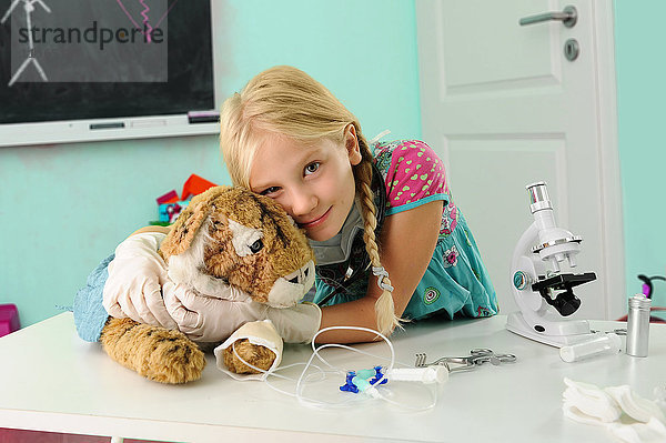 Porträt eines Mädchens  das sich als Tierarzt ausgibt und Spielzeugtiger mit intravenösem Tropf umarmt