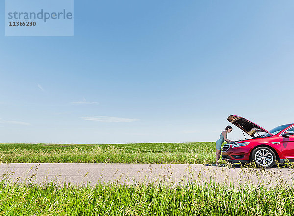 Frau schaut unter die Motorhaube eines kaputten Autos