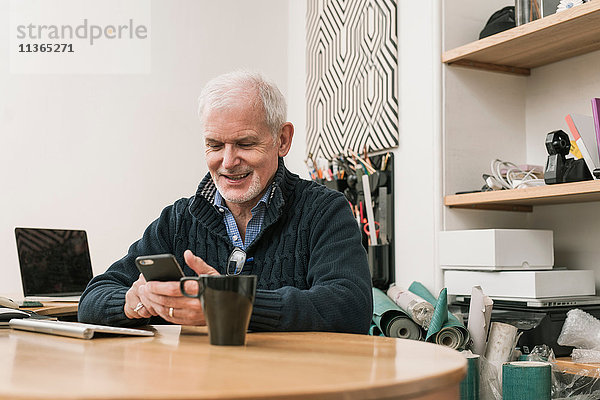Älterer Mann lächelt  benutzt Mobiltelefon am Arbeitstisch