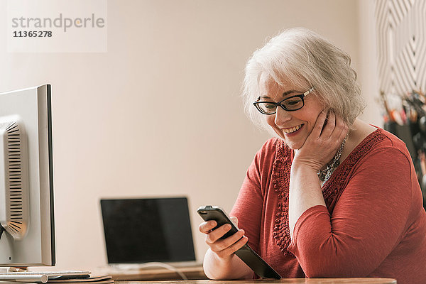 Lächelnde Frau  die ein Mobiltelefon am Schreibtisch benutzt