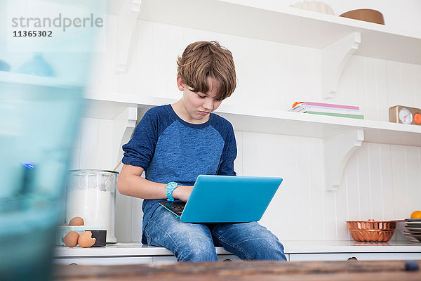 Junge sitzt auf der Küchenarbeitsfläche und benutzt einen Laptop