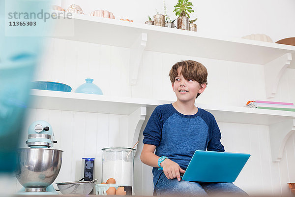 Junge sitzt auf der Küchenarbeitsfläche und benutzt einen Laptop