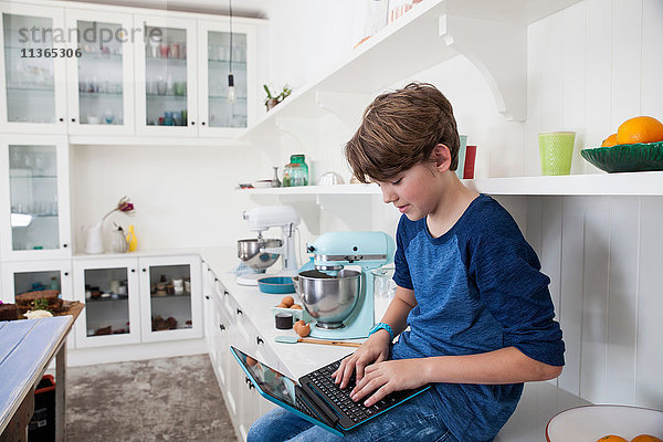 Junge sitzt auf der Küchenarbeitsfläche und benutzt einen Laptop
