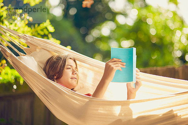 Teenager-Junge entspannt in der Gartenhängematte beim Lesen eines Buches