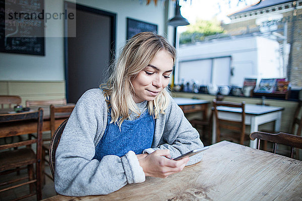 Junge Frau im Cafe sitzend  mit Smartphone  lächelnd