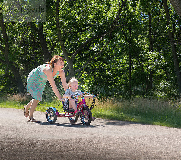 Mutter schiebt Tochter auf Dreirad