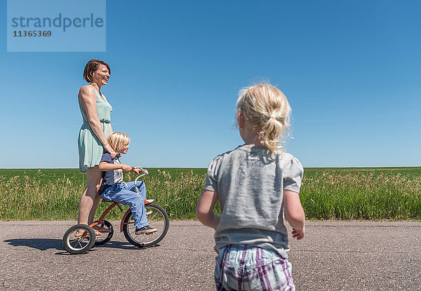 Mutter und Kinder fahren Dreirad in ländlicher Gegend