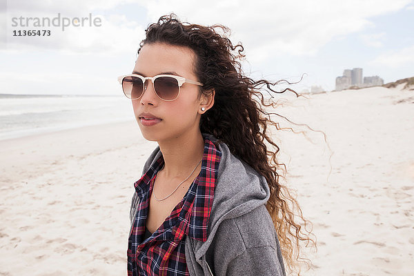 Junge Frau mit Sonnenbrille spaziert allein am windigen Strand  Western Cape  Südafrika