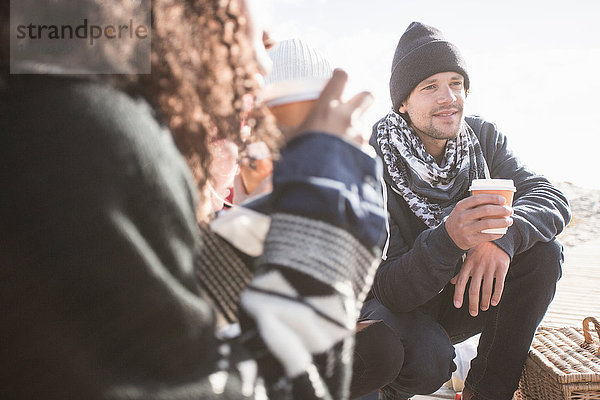 Junge erwachsene Freunde kauern am Strand mit Kaffee zum Mitnehmen  Western Cape  Südafrika