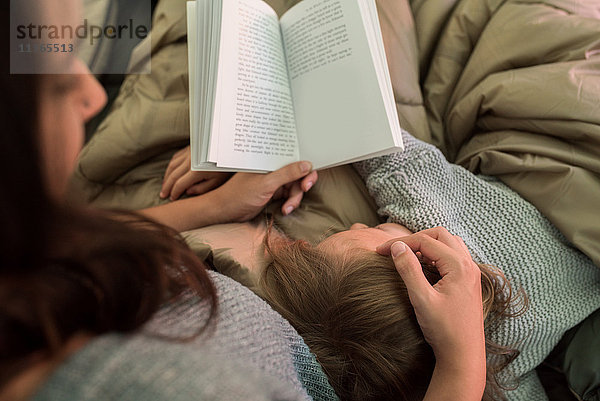 Junges Mädchen schläft auf seiner Mutter  während ihre Mutter ein Buch liest  Rückansicht