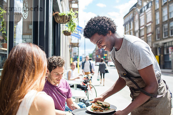 Kellner serviert Mittagessen zu Paar in der Stadt Bürgersteig Cafe