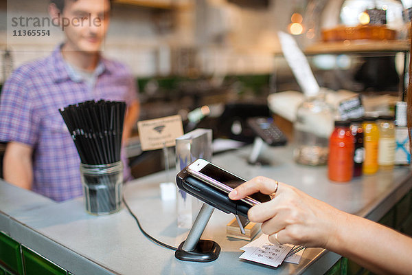 Abgeschnittene Aufnahme einer Kundin mit kontaktlosem Bezahlen per Smartphone im Café