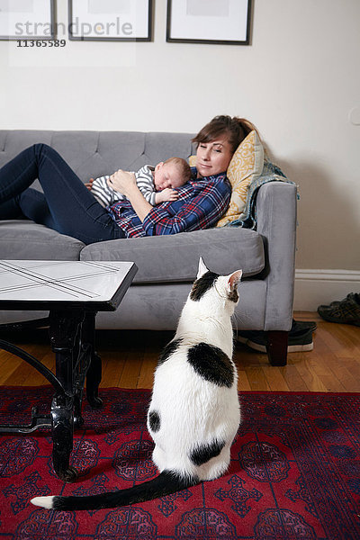 Mutter und kleiner Junge liegen auf dem Sofa und schauen die Katze an