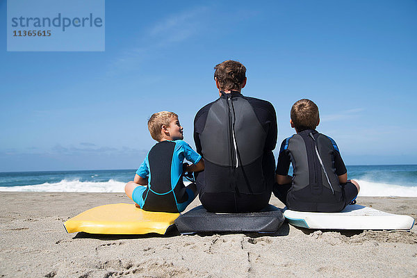 Rückansicht eines Mannes und zweier Söhne auf Bodyboards sitzend  Laguna Beach  Kalifornien  USA