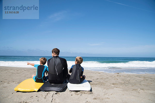Rückansicht eines Mannes und zweier Söhne  die auf Bodyboards sitzen und nach vorne zeigen  Laguna Beach  Kalifornien  USA