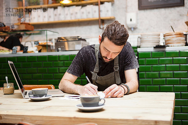 Junge männliche Kaffeehausbesitzerin bei Tisch