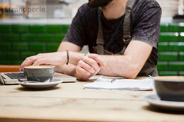 Ausschnitt eines männlichen Cafébesitzers  der am Tisch Papierkram erledigt.