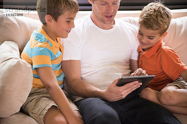 Mann und zwei Söhne benutzen digitales Tablett auf dem Sofa