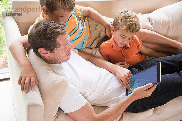 Mann und zwei Söhne benutzen digitalen Tablet-Touchscreen auf dem Sofa