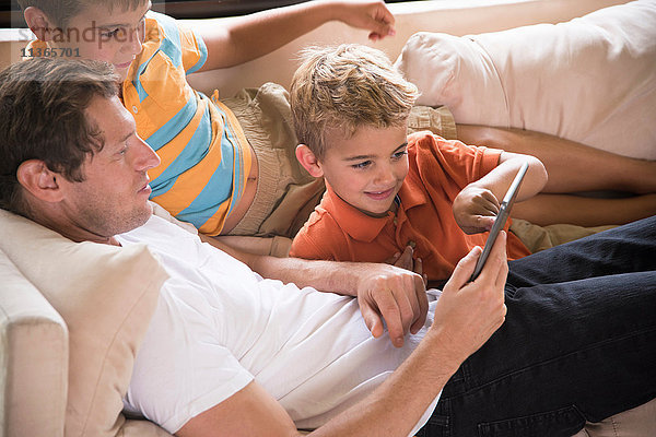 Mann und zwei Söhne zeigen auf digitales Tablett auf dem Sofa