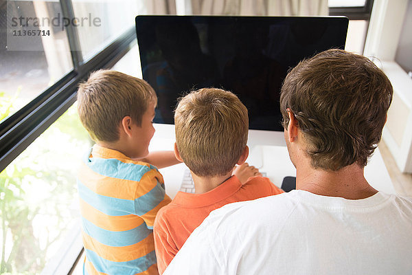 Rückansicht von Mann und zwei Söhnen mit Desktop-Computer