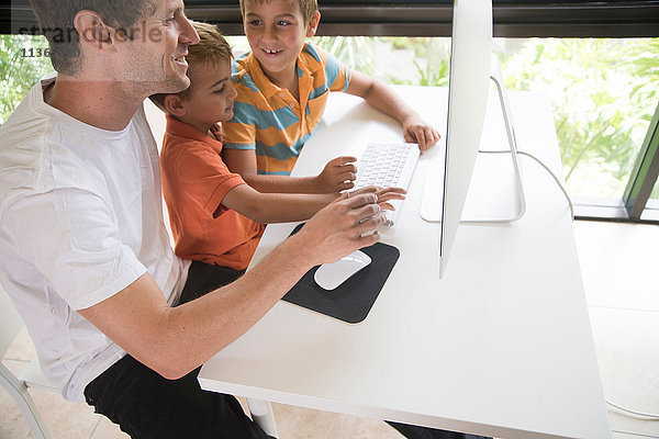 Mann  der zwei Söhnen zeigt  wie man einen Desktop-Computer benutzt.