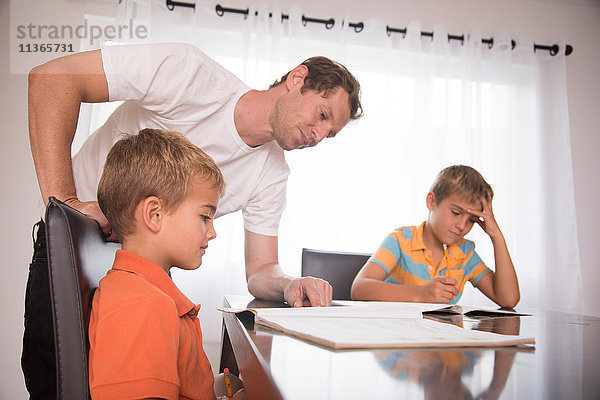 Mann berät zwei Söhne bei den Hausaufgaben am Tisch