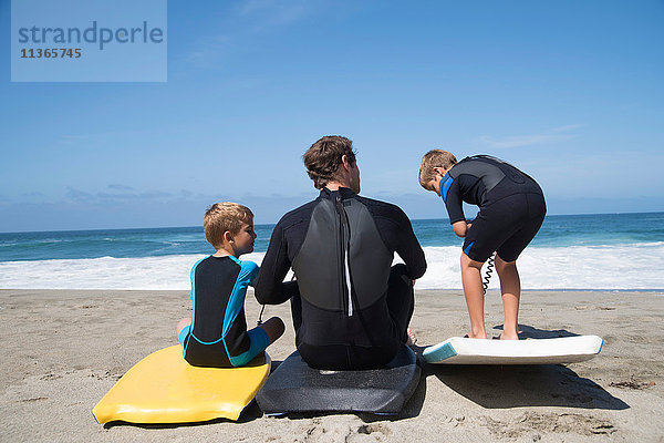 Rückansicht von Vater und zwei Söhnen beim Üben mit Bodyboards am Strand  Laguna Beach  Kalifornien  USA