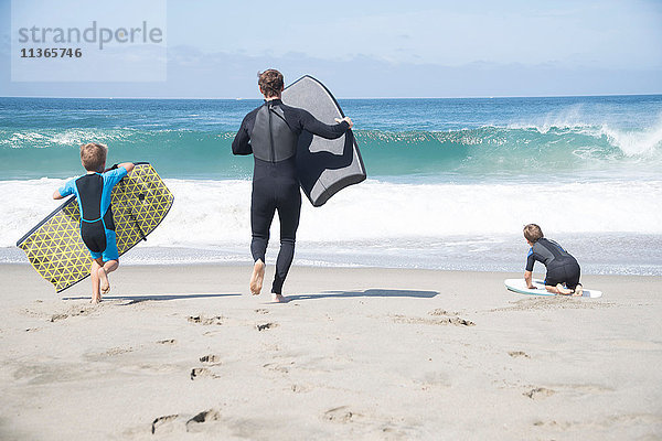Rückansicht von Vater und zwei Söhnen  die mit Bodyboards am Strand laufen  Laguna Beach  Kalifornien  USA