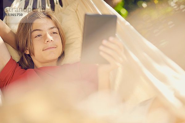 Teenager-Junge entspannt in der Gartenhängematte beim Durchblättern der digitalen Tablette