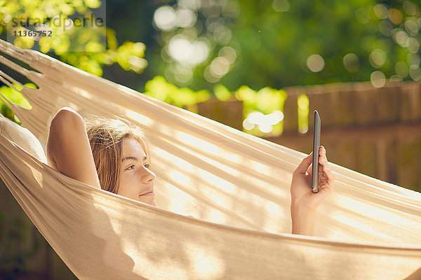 Jugendlicher Junge  der in der Gartenhängematte liegt  die digitale Tablette grast