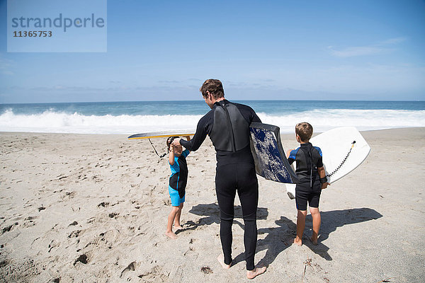 Rückansicht eines Vaters und zweier Söhne  die sich am Strand auf Bodyboarding vorbereiten  Laguna Beach  Kalifornien  USA