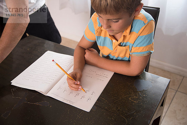 Junge mit Vater beim Schreiben im Hausaufgabenbuch am Tisch