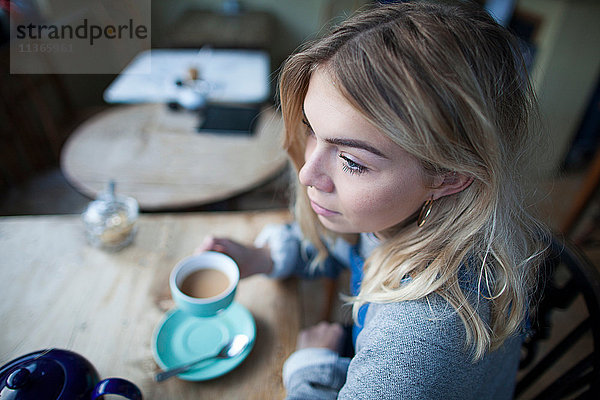 Junge Frau sitzt im Café  hält Teetasse  nachdenklicher Gesichtsausdruck