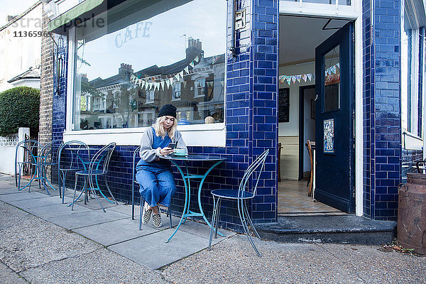 Junge Frau  die vor dem Café sitzt  mit dem Smartphone