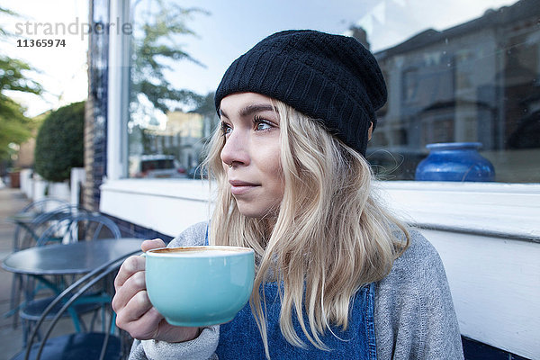 Junge Frau sitzt vor dem Café und trinkt eine Tasse Tee.