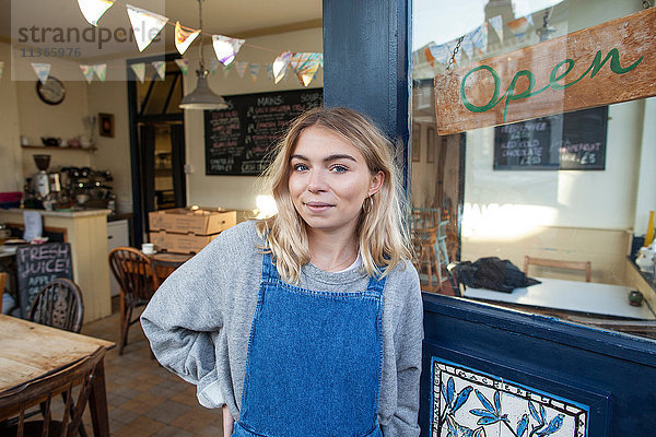 Porträt einer jungen Frau  die in der Tür eines Cafés steht