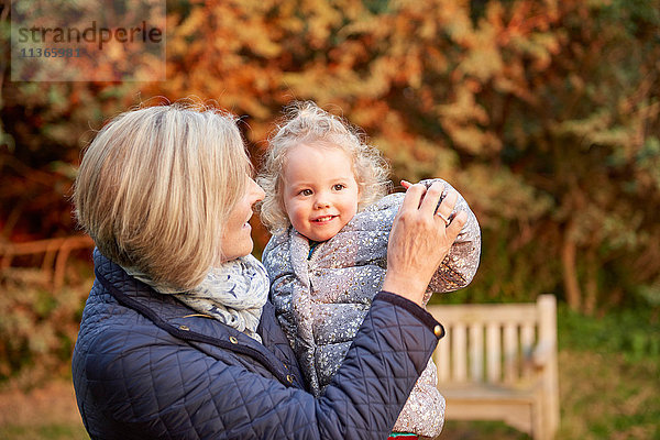 Ältere Frau trägt Kleinkind-Enkelin im Herbstpark
