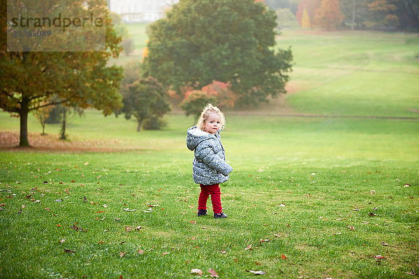 Porträt eines weiblichen Kleinkindes  das im Herbst im Park über die Schulter schaut