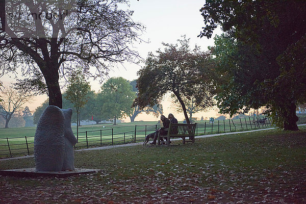Silhouettenansicht einer älteren Frau und ihrer Tochter  die auf einer Parkbank im Herbstpark sitzen