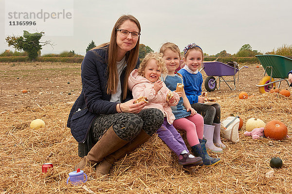 Porträt einer mittleren erwachsenen Frau und dreier Mädchen beim Picknick im Kürbisfeld