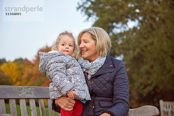 Ältere Frau sitzt mit Kleinkind-Enkelin im Herbstpark