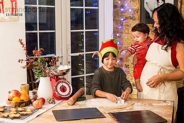 Reife Frau bereitet mit Söhnen an der Küchentheke Weihnachtsplätzchen zu