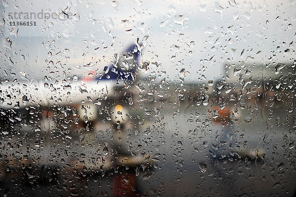 Fensteransicht eines im Regen auf dem Flughafen-Vorfeld geparkten Flugzeugs