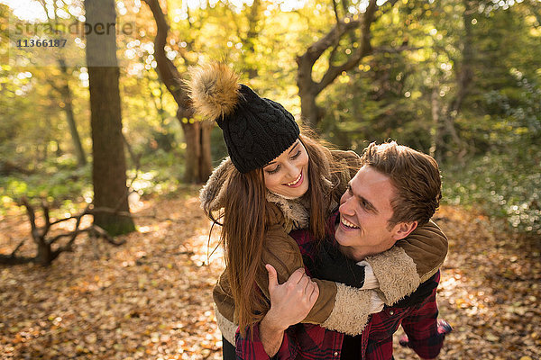 Junges Paar im Wald  junger Mann gibt junger Frau Huckepack  lachend