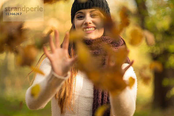 Junge Frau wirft Herbstblätter in die Luft und lächelt