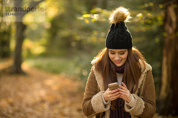 Junge Frau im Wald  schaut auf Smartphone und lächelt