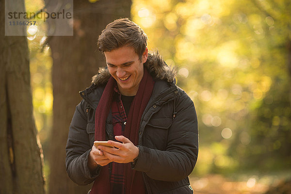 Junger Mann im Wald  schaut auf Smartphone und lächelt