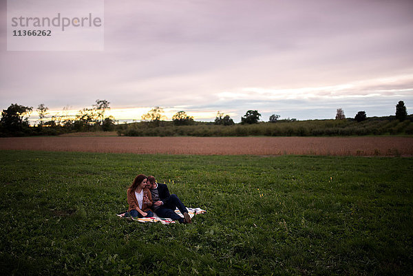 Romantisches Paar entspannt sich bei Sonnenuntergang auf einer Picknickdecke im Feld