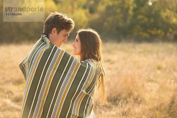 Junges Paar in ländlicher Umgebung  in eine Decke gewickelt  von Angesicht zu Angesicht  lächelnd